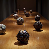 CARLOS RUNCIE TANAKA, "Huayco / Kawa / Río", 2003-2006, Variable dimensions, Fragments of dinnerware, stoneware – multiple firings in gas kiln, 1300ºC., Diameter of each sphere: 60 cm. Ceramic fragments produced between years 1988 and 2005, broken in the kiln and used to create new spherical forms. The artist associates this production to the ritual abandon made by Japanese Master Potters of broken pieces of pottery that are thrown away into the river.